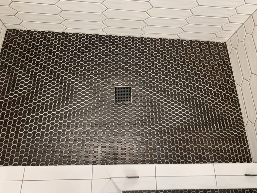 Black hexagon mosaic shower pan meeting white picket walls